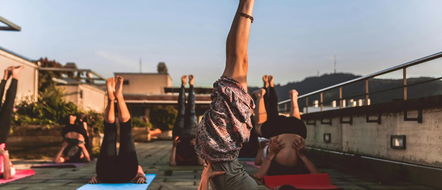pexels-amin-sujan-529242-1375883.jpg Menschen üben auf Yoga-Matten im Freien den Schulterstand, umgeben von Natur und Abendstimmung.