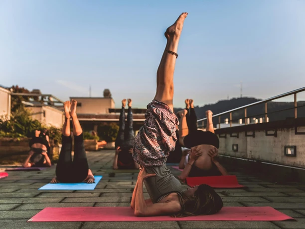 pexels-amin-sujan-529242-1375883.jpg Menschen üben auf Yoga-Matten im Freien den Schulterstand, umgeben von Natur und Abendstimmung.