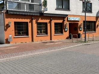 Rotes Gebäude mit großen Fenstern und Eingangsschild "Hellas", griechisches Restaurant in der Stadt.