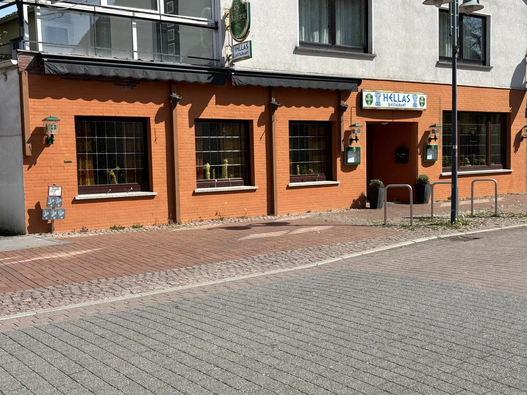 Rotes Gebäude mit großen Fenstern und Eingangsschild "Hellas", griechisches Restaurant in der Stadt.