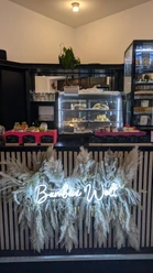 PXL_20241108_103529933.jpg Ein kleiner Verkaufsstand bietet Gebäck und Snacks an, dekoriert mit leuchtendem Schriftzug "Bambi Welt".