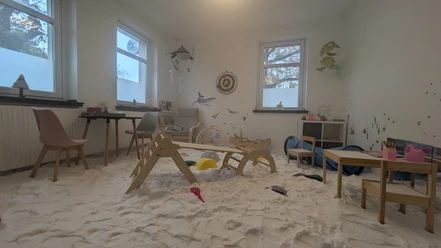 PXL_20241108_105349038.jpg Ein Kinderzimmer mit Spielsachen, Sandboden und Wanddekorationen von Meerestieren in sanftem Licht.