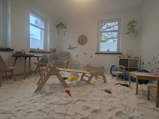 PXL_20241108_105349038.jpg Ein Kinderzimmer mit Spielsachen, Sandboden und Wanddekorationen von Meerestieren in sanftem Licht.