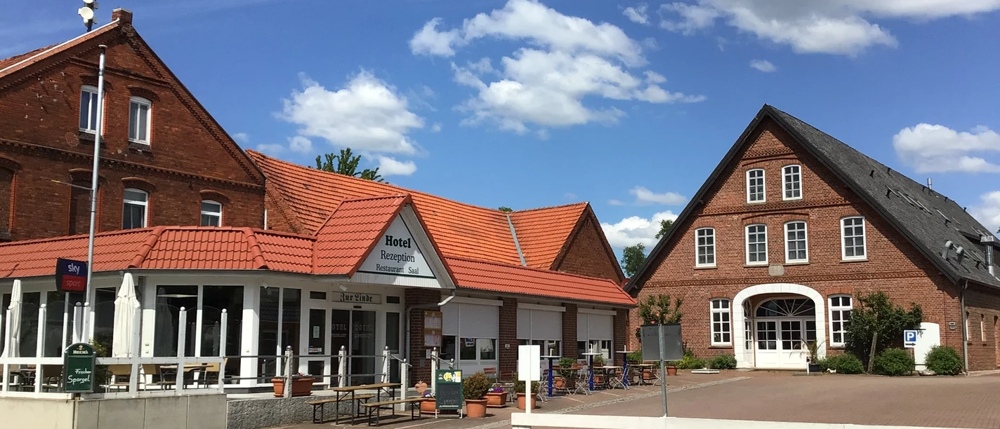 Traditioneel plattelandshotel met vakwerkarchitectuur, omgeven door een gezellig terras en blauwe luchten.