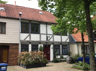 Vakwerkhuis in de Domstraße voor groene bomen, rode dakpannen en lichtgekleurde luiken.