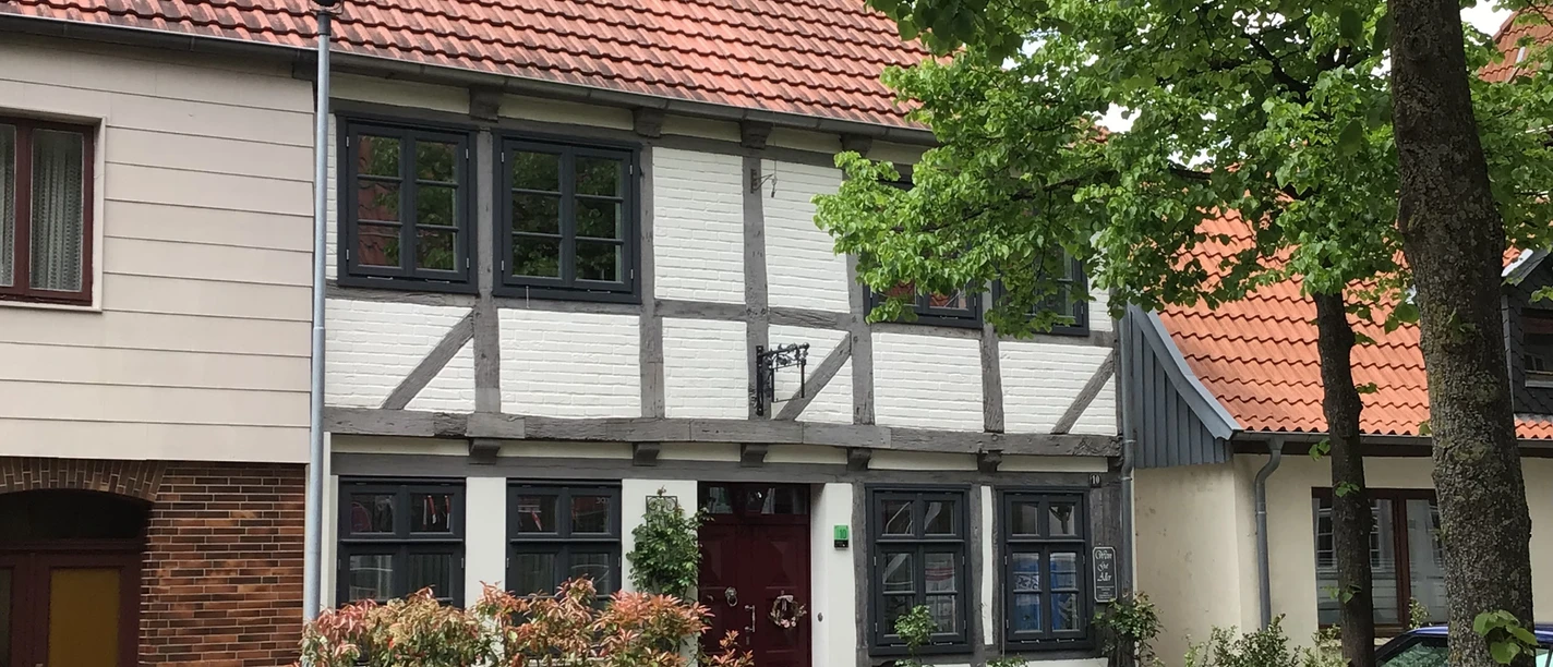 Vakwerkhuis in de Domstraße voor groene bomen, rode dakpannen en lichtgekleurde luiken.