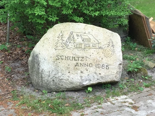 Reiterhof Schultz: Großer Stein mit Gravur eines Hauses und Tannen, darüber "Schultz Anno 1986".