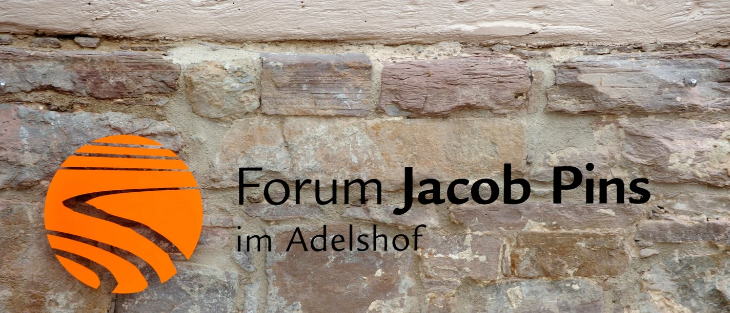 bild_pins_vakalender Forum Jacob Pins Schriftzug mit Logo auf einer rustikalen Bruchsteinmauer.