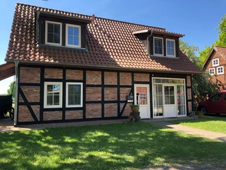 Vakwerkhuis met rode bakstenen en zwarte houten stijlen, omgeven door een groen gazon en blauwe lucht.