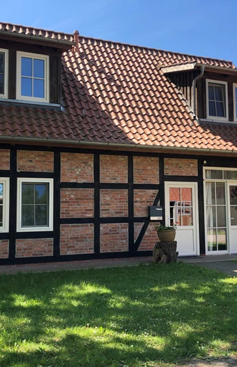 Fachwerkhaus mit roten Ziegeln und schwarzen Holzstreben, umgeben von grünem Rasen und blauen Himmel.Half-timbered house with red bricks and black wooden struts, surrounded by a green lawn and blue sky.Bindingsværkshus med røde mursten og sorte træstivere, omgivet af en grøn græsplæne og blå himmel.Vakwerkhuis met rode bakstenen en zwarte houten stijlen, omgeven door een groen gazon en blauwe lucht.