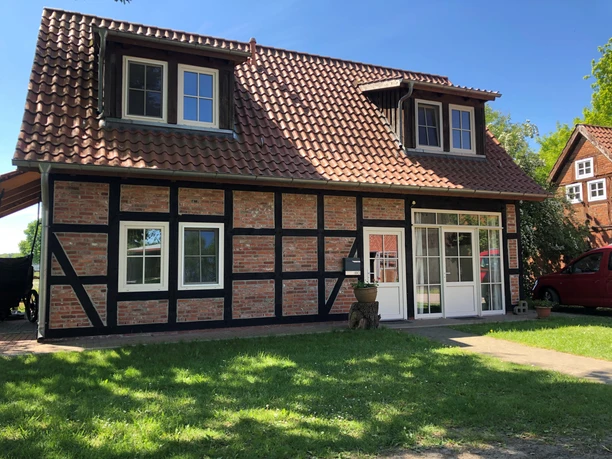 Fachwerkhaus Bruchhausen Fachwerkhaus mit roten Ziegeln und schwarzen Holzstreben, umgeben von grünem Rasen und blauen Himmel.