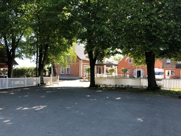 Embedded in trees, a brick house of a riding stable with a white fence and courtyard can be seen.
