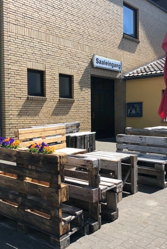 Außenbereich von Döhlings Gasthaus mit rustikalen Sitzmöbeln aus Paletten und einem Sonnenschirm.