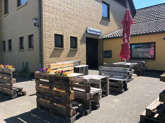 Döhlings Gasthaus Außenbereich von Döhlings Gasthaus mit rustikalen Sitzmöbeln aus Paletten und einem Sonnenschirm.