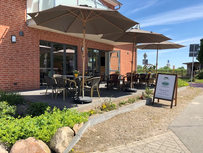 Ein Café mit Außenbereich und markanten Sonnenschirmen vor einem Backsteingebäude unter blauem Himmel.