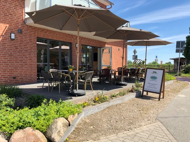 Hof Kuck Ein Café mit Außenbereich und markanten Sonnenschirmen vor einem Backsteingebäude unter blauem Himmel.