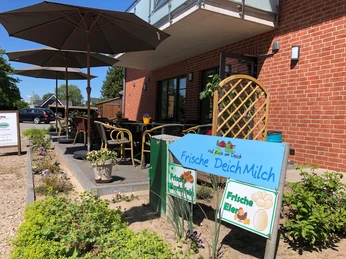 Ein rotes Backsteingebäude mit Terrasse, Gartenmöbeln und Schildern für lokale Milch und Eier.