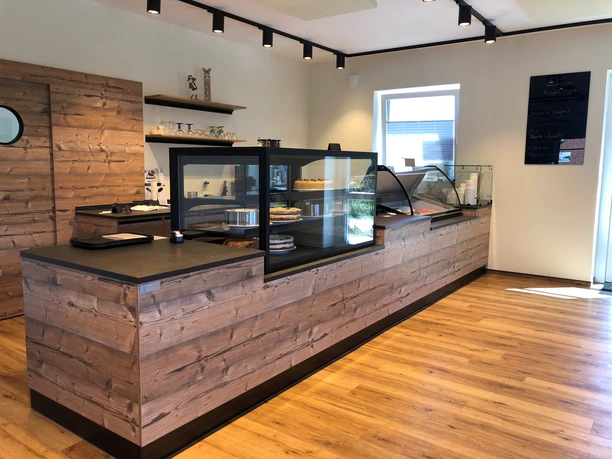 Hof Kuck Ein heller Verkaufsraum mit einer langen Theke aus Holz und Glasauslagen voller frischer Kuchen.