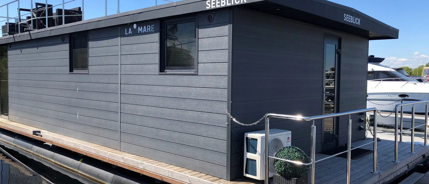 La Mare Hausboot Wieltsee Houseboat with modern design and roof terrace on calm waters under a clear blue sky.