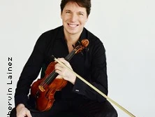 Ein Musiker in schwarzem Outfit hält eine Violine und lächelt freundlich in die Kamera.