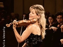 Eine Violinistin spielt konzentriert auf der Bühne, begleitet von einem Orchester im Hintergrund.