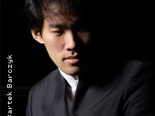 Ein Mann asiatischer Herkunft in schwarzer Kleidung, der ernsthaft in die Ferne blickt.