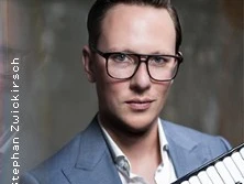 Ein Mann mit Brille in blauem Anzug hält ein Akkordeon, fotografiert von Stephan Zwickirsch.