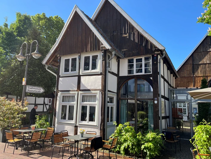 Museumscafé Gütersloh Fachwerkhaus mit Café-Terrasse, umgeben von grüner Bepflanzung und klarem Himmel.