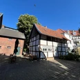 Innenhof Museumscafé Güterloh Fachwerkhäuser in einem sonnigen Innenhof, umgeben von Backsteinbauten und grünen Bäumen.