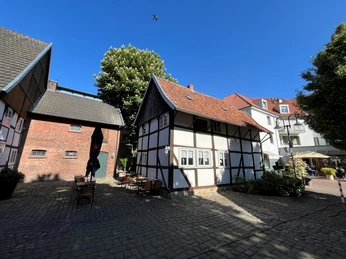 Innenhof Museumscafé Güterloh Fachwerkhäuser in einem sonnigen Innenhof, umgeben von Backsteinbauten und grünen Bäumen.