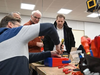 repair-cafe-bad-zwischenahn-besuch-buergermeister.jpg Menschen konzentrieren sich engagiert auf die Reparatur eines Geräts, mit neugierigen Zuschauern.