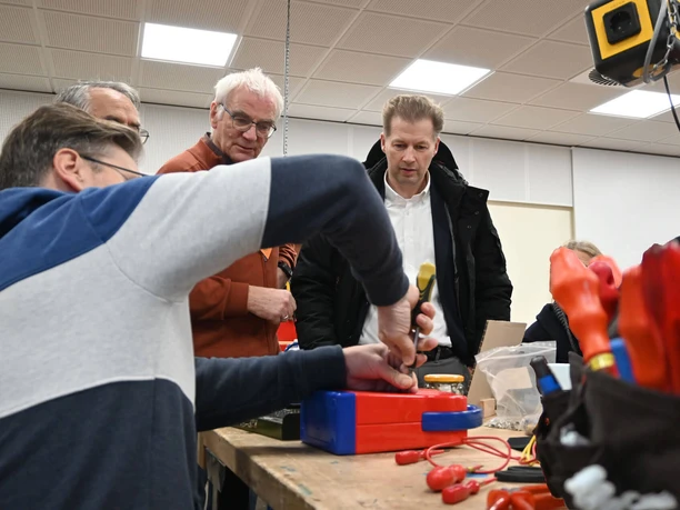 repair-cafe-bad-zwischenahn-besuch-buergermeister.jpg People are focused on repairing an appliance, with curious onlookers.