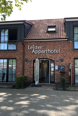 Backstein-Fassade mit zwei Stockwerken, zentralem Eingang und überdachter Terrasse mit Sitzgelegenheiten.