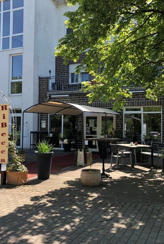 RiBecca-Hotel Das RiBecca-Hotel mit moderner Architektur, einem einladenden Eingangsbereich und grüner Bepflanzung.