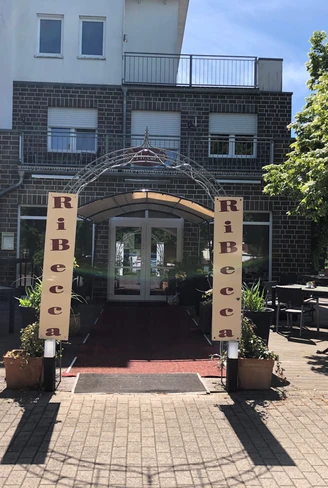 RiBecca-Hotel Der Eingangsbereich des RiBecca-Hotels mit Markise und Pflanzen, umgeben von Bäumen.