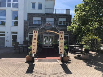 RiBecca-Hotel Der Eingangsbereich des RiBecca-Hotels mit Markise und Pflanzen, umgeben von Bäumen.The entrance area of the RiBecca Hotel with awning and plants, surrounded by trees.Indgangspartiet til RiBecca Hotel med markise og planter, omgivet af træer.De ingang van het RiBecca Hotel met luifel en planten, omringd door bomen.