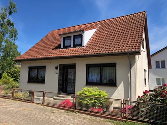 Een vrijstaand huis met een rood zadeldak, omringd door struiken en een speelse voortuin.