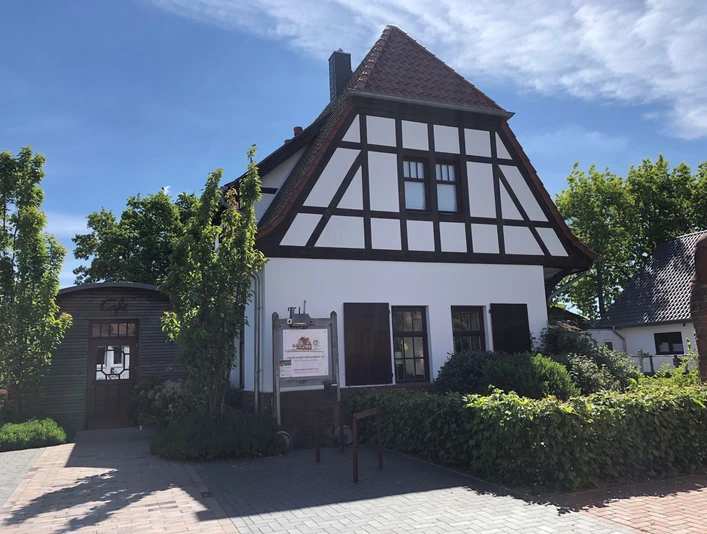 Fachwerkgebäude am Sudweyher Bahnhof, von Bäumen umgeben und unter klarem, blauem Himmel.
