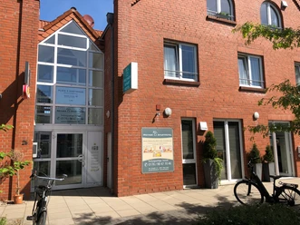 Weyher Aparthotel Eingang eines roten Backsteingebäudes mit Glasfassade, außen Fahrräder und grüne Pflanzen.