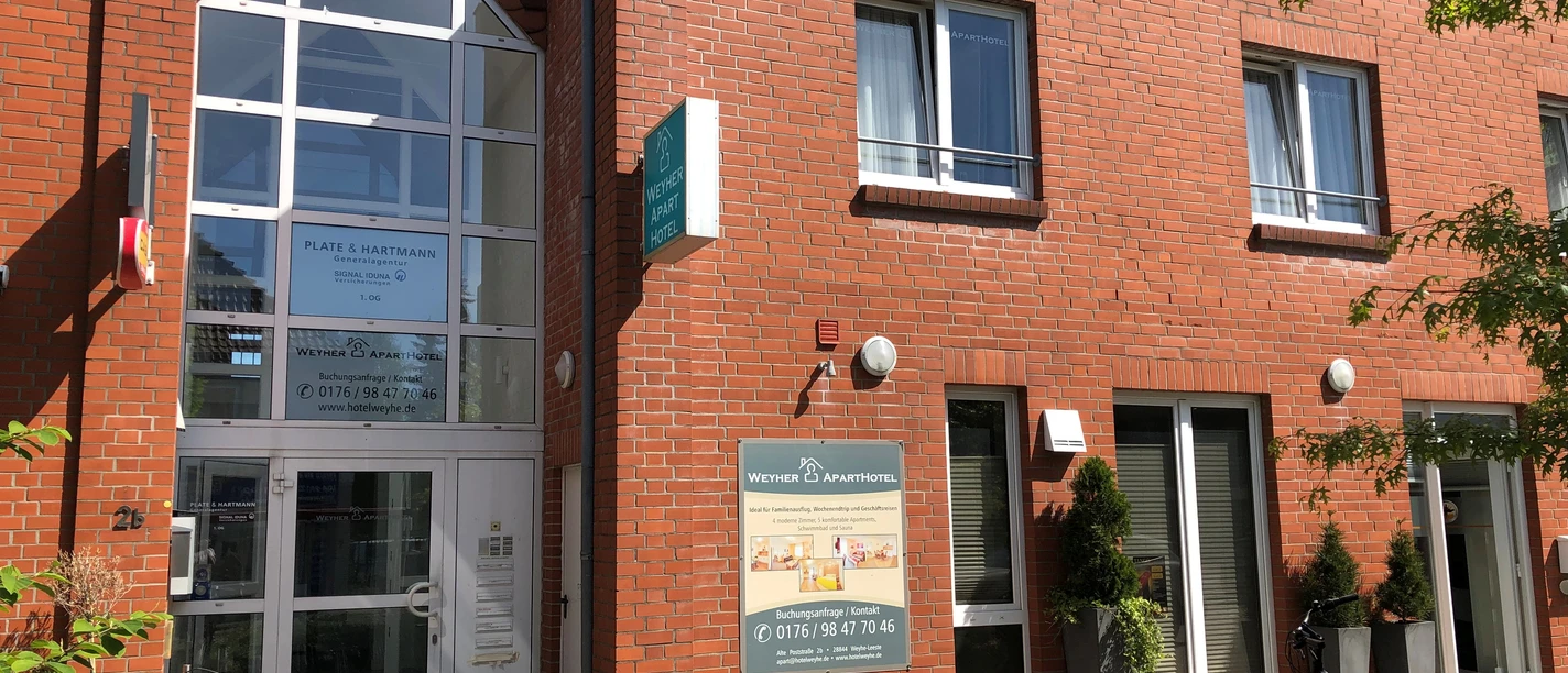 Weyher Aparthotel Eingang eines roten Backsteingebäudes mit Glasfassade, außen Fahrräder und grüne Pflanzen.