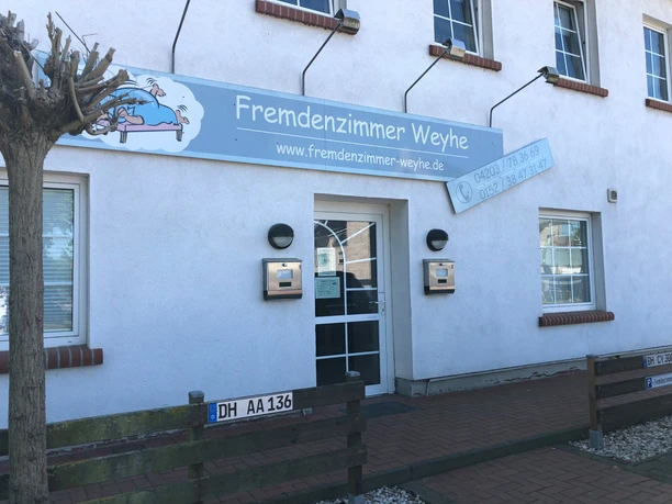 Entrance of a bright building with a sign "Fremdenzimmer Weyhe" and two mailboxes.