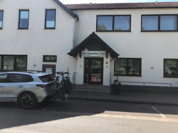 Entrance area of a hotel with a sign "Kirchweyher Hof" above the door, bicycle rack on car.