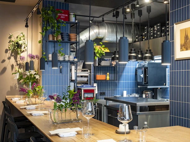 Pottkind Elegant, modern kitchen in the restaurant with blue-tiled walls; set wooden tables decorated with fresh flowers.