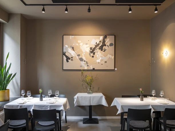 Pottkind In a stylishly decorated restaurant, two set tables stand in front of a wall displaying abstract art.