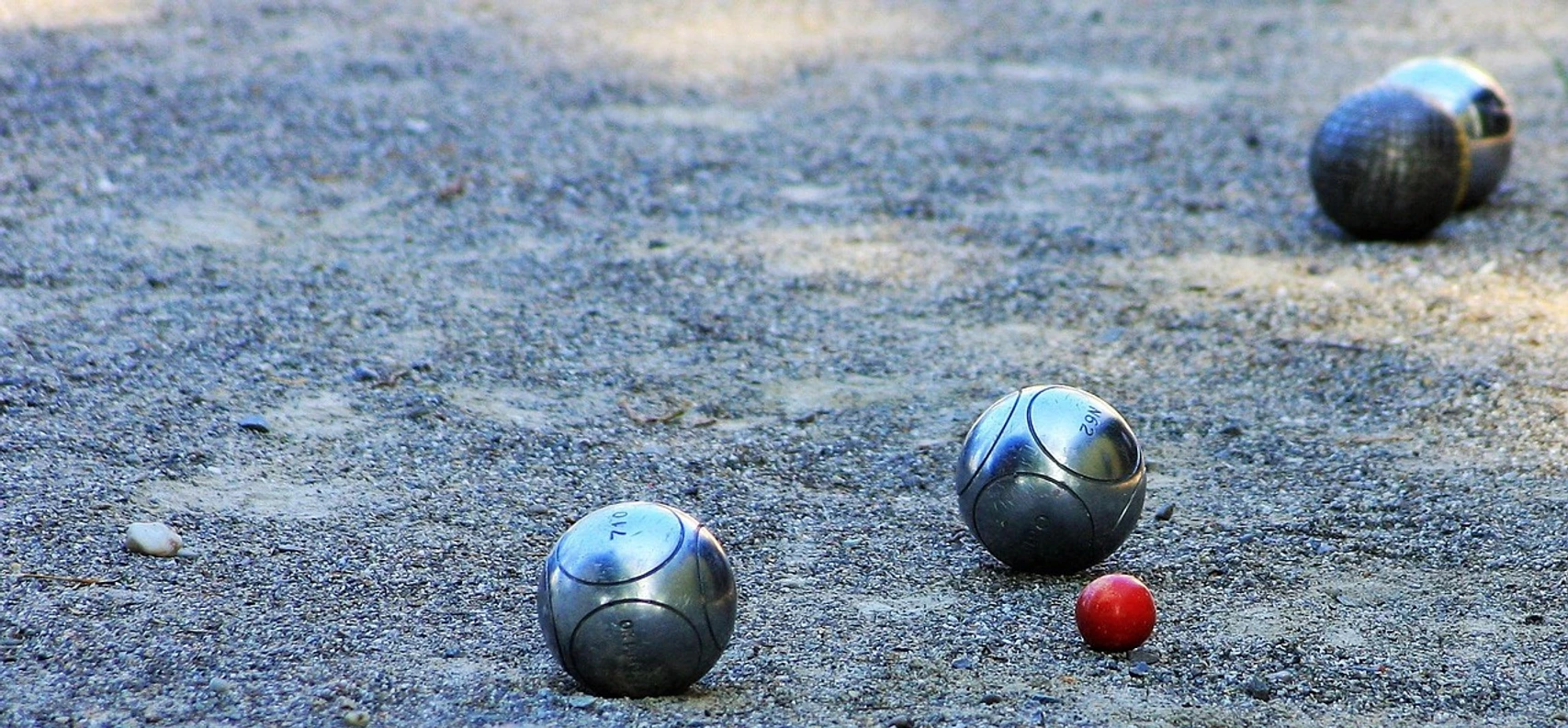 Boulefeld Mehrere Boulekugeln liegen verstreut auf einem sandigen Spielfeld unter freiem Himmel.