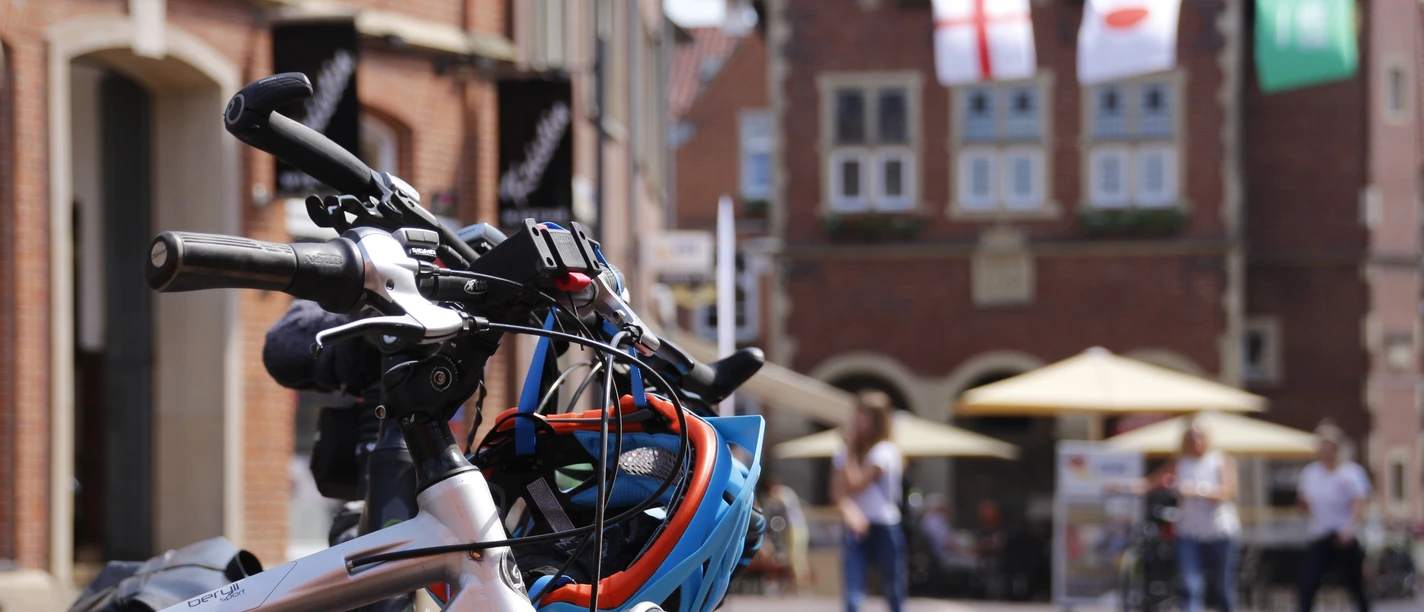 Fahrrad in Meppener Innenstadt ©Emsland Tourismus GmbH (3).jpg Fahrrad mit Helm in sonniger Innenstadt von Meppen, Passanten und historische Fassaden im Hintergrund