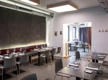 maiBeck Modernes Restaurantinterieur mit schlichten Tischen, eleganten grauen Stühlen und dezenten Wanddekorationen.Modern restaurant interior featuring minimalist tables, elegant grey chairs, and subtle wall decorations.