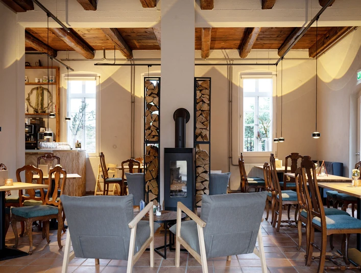 001_Alte-Remise_Urheber_Top-Light.jpg Ein stimmungsvoller Innenraum mit Holzmöbeln, einer zentralen Holzsäule und moderner Beleuchtung.
