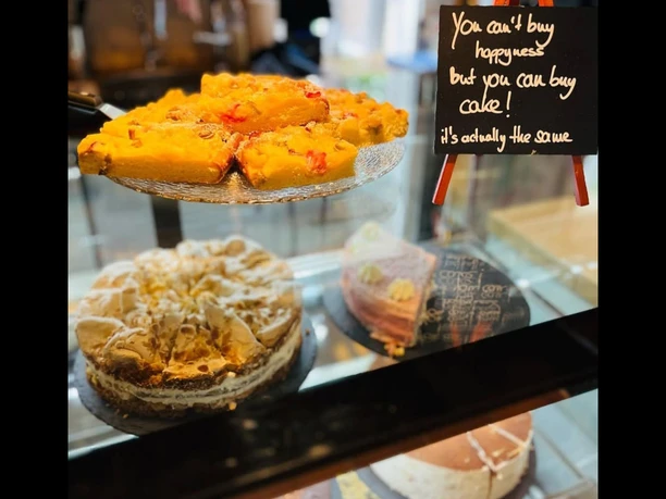 Eine Glasvitrine präsentiert bunte Kuchen und Torten; ein Schild sagt, Kuchen bringt Glück.