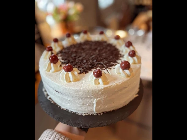 Schwarzwälder Kirschtorte mit Sahnetupfern und Kirschen, dekoriert mit Schokoladenspänen obenauf.